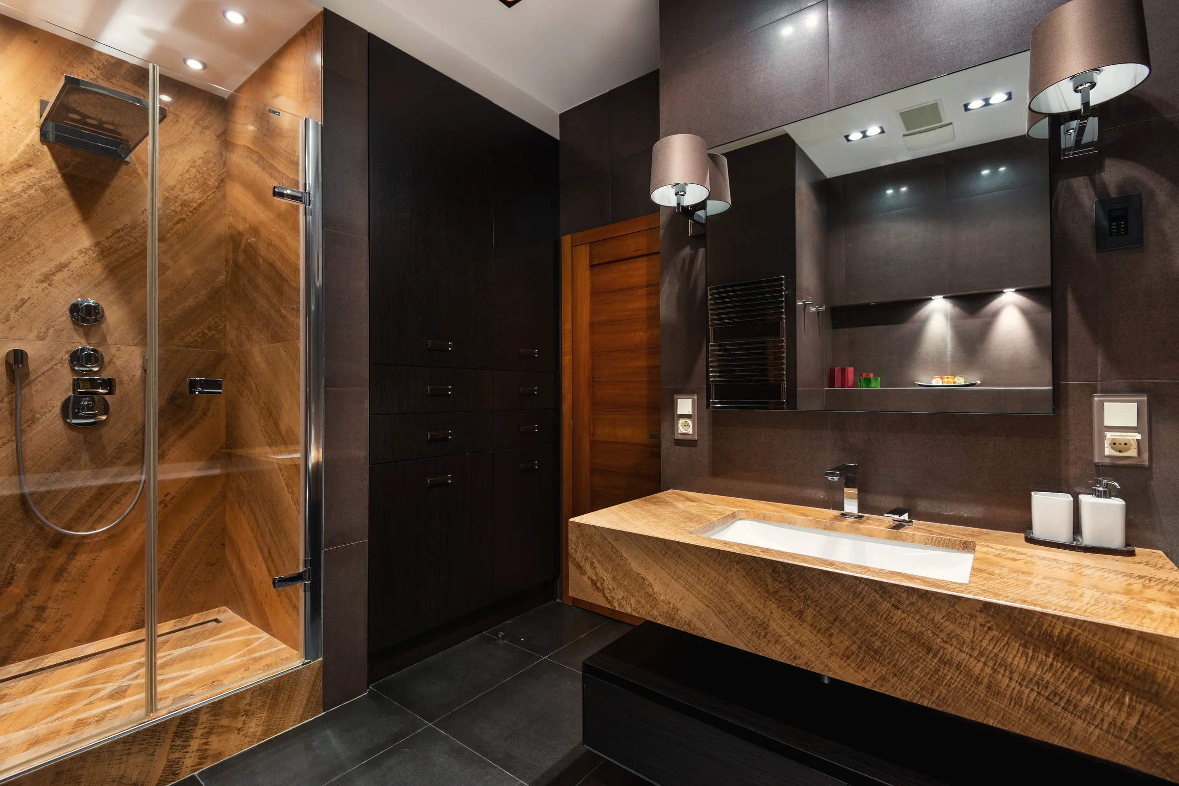 Example bathroom: a floating stone vanity with shaded wall lights beside the mirror, and a stone-lined walk-in shower.