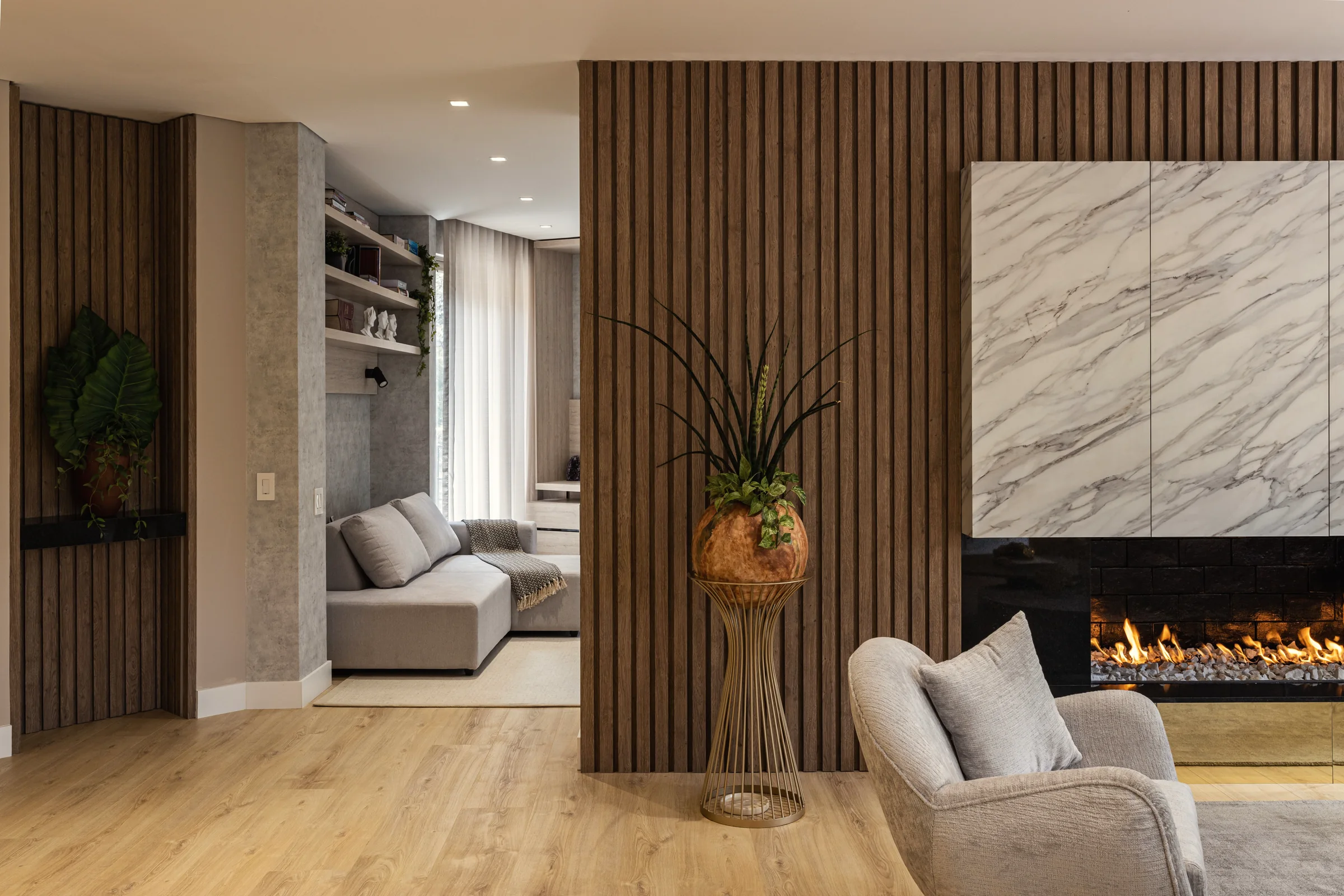 Example living room: a fluted timber wall, a veined stone fireplace with a linear fire, and a lounge with built-in shelving beyond.